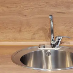 Okrągły zlew kuchenny ze stali nierdzewnej z chromowaną baterią na tle drewnianego blatu.
