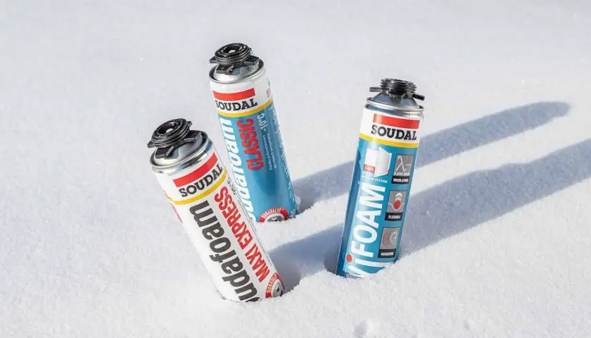 Trzy puszki pianki montażowej zimowej Soudal w śniegu. Pianka "Maxi Express" i "Classic" obok siebie, a dalej "Foam".