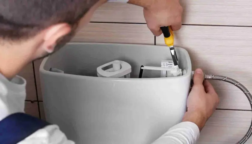 Mężczyzna naprawia mechanizm spłuczki toaletowej za pomocą narzędzia.