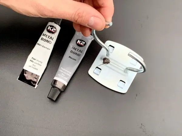 Dwie tubki kleju do blachy K2 Metal Bond (żywica i utwardzacz) oraz metalowy element z nałożonym klejem.